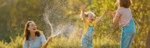 mom spraying hose on jumping children in sun happy