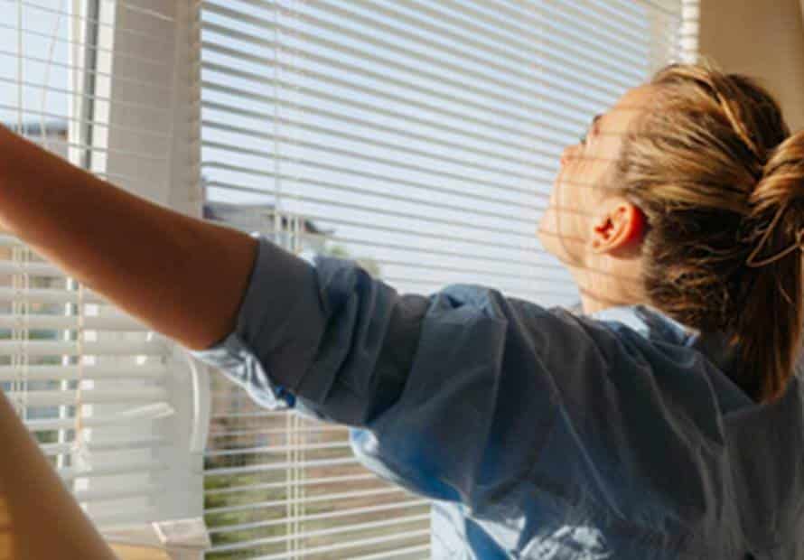 Woman opening blinds to sunshine